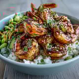 Freshly grilled shrimp glistens atop steamed jasmine rice, garnished with edamame, cucumbers, and sesame seeds for a vibrant Asian shrimp bowl.
