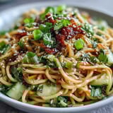 Refreshing cold sesame noodle bowl featuring chilled wheat noodles, crisp cucumber, and zesty sesame dressing, topped with fresh herbs.