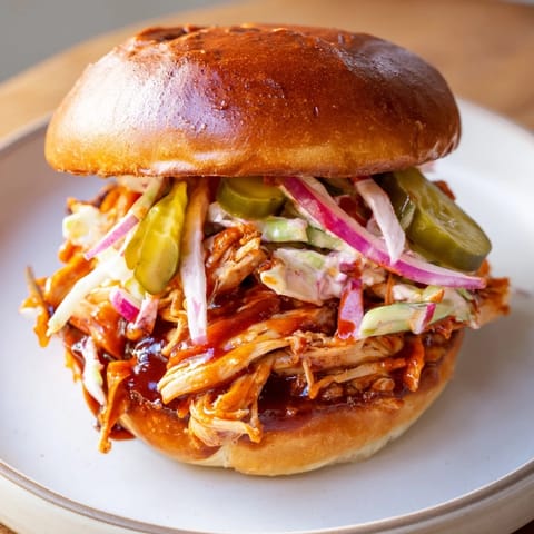 A close-up of a perfectly constructed BBQ chicken sandwich, served warm, with a tangy barbecue sauce.