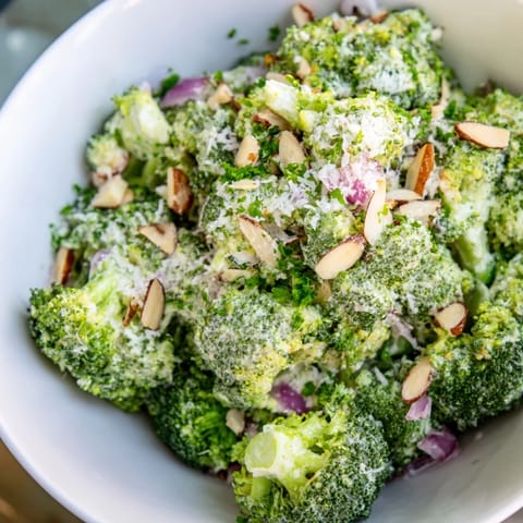 Fresh Garlic Parmesan Broccoli Salad served chilled in a white bowl, topped with shaved Parmesan and chopped parsley, perfect for potlucks.