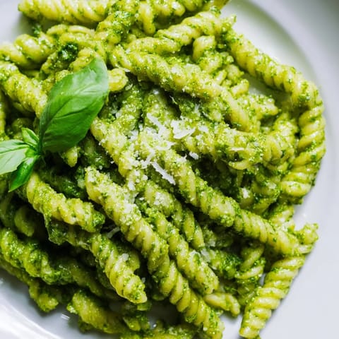 Steaming bowl of creamy sunflower seed pesto pasta with a vibrant green sauce, paired with a glass of white wine.