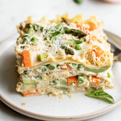 Layered Spring Veggie Alfredo Lasagna served on a white plate, garnished with fresh basil leaves.