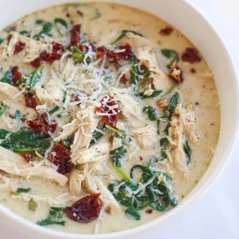 Close-up of Creamy Tuscan Chicken Soup, showing tender shredded chicken, vibrant spinach, and creamy broth infused with sun-dried tomatoes.
