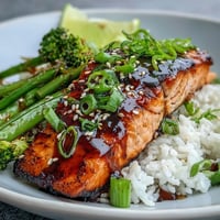 Flaky maple soy glazed salmon rests on a bed of fluffy jasmine rice alongside crisp-tender broccoli, snap peas, and red bell peppers.