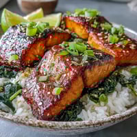 Overhead view of a Miso Glazed Salmon Bowl featuring flaky salmon atop jasmine rice and wilted spinach with ginger.